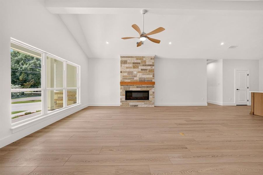 Spacious living area featuring wood-finish flooring, a stone-clad fireplace with a wood mantel, a ceiling fan, and large picture windows