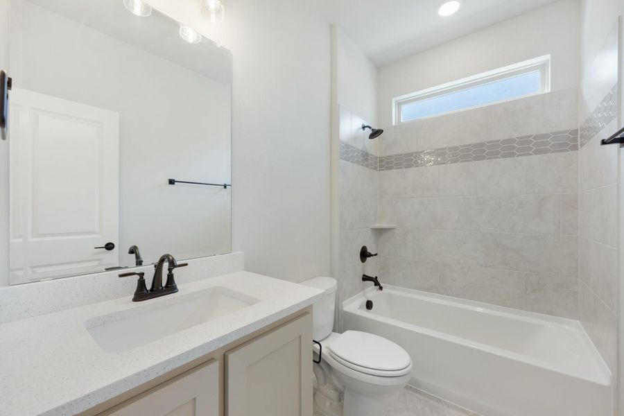 Bathroom with white quartz vanity, tiled shower-tub combo, and dark bronze fixtures