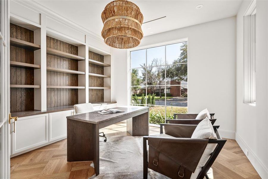 This elegant study features glass French doors, a large picture window with scenic south lawn views, and custom built-ins with Emtek Mod Hex brass pulls. White oak hardwood floors with a custom design add character, while a Drew & Jonathan Thurlo hanging shade brings warmth.