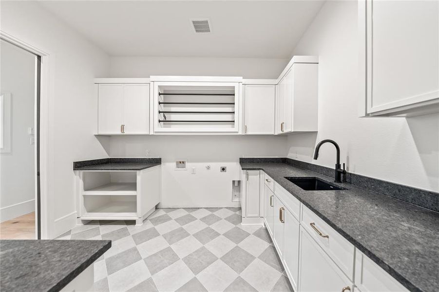 Laundry room featuring extensive white cabinetry, dark countertops, a black sink with a matte black faucet, and patterned floor tiling