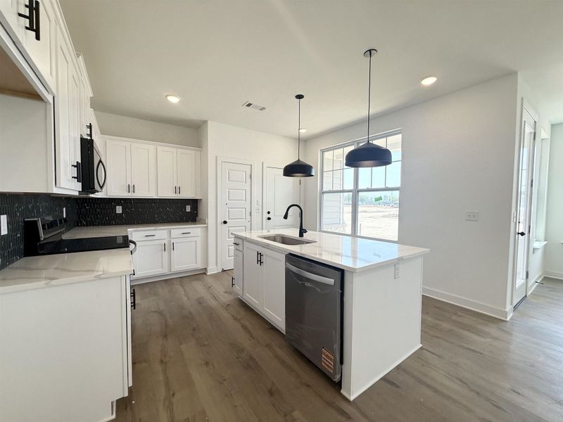Kitchen featuring white cabinetry, a center island with sink, light stone countertops, and dishwasher