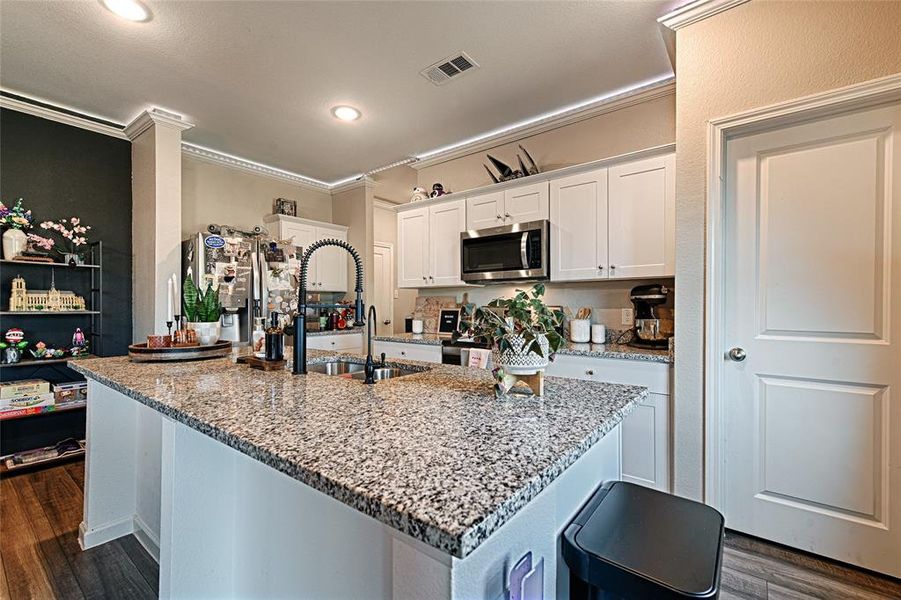 Kitchen with white cabinets, crown molding, light stone countertops, dark wood-style flooring, and stainless steel appliances Kitchen with white cabinets, crown molding, light stone countertops, dark wood-style flooring, and stainless steel appliances