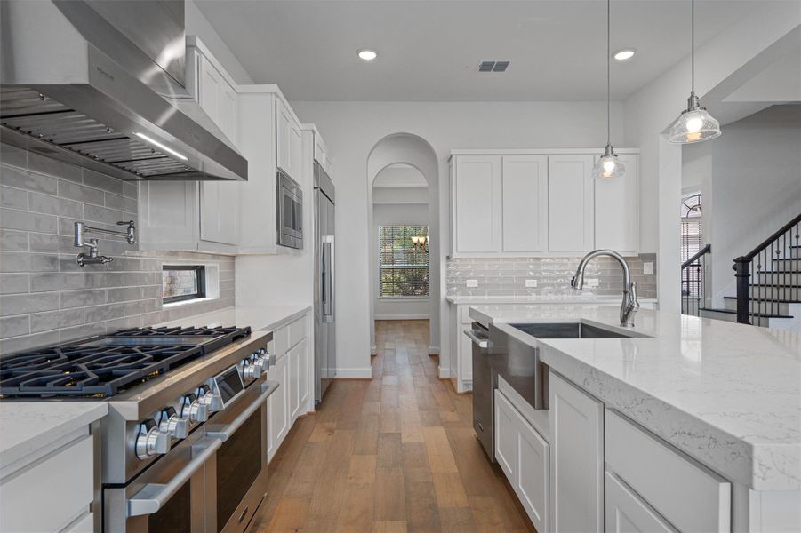 Modern kitchen featuring stainless steel appliances, white cabinetry, light-toned wood-finish flooring, a pot filler faucet, and a large kitchen island with an undermount sink