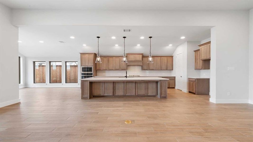 Kitchen with built in microwave, pendant lighting, oven, a kitchen island with sink, and backsplash