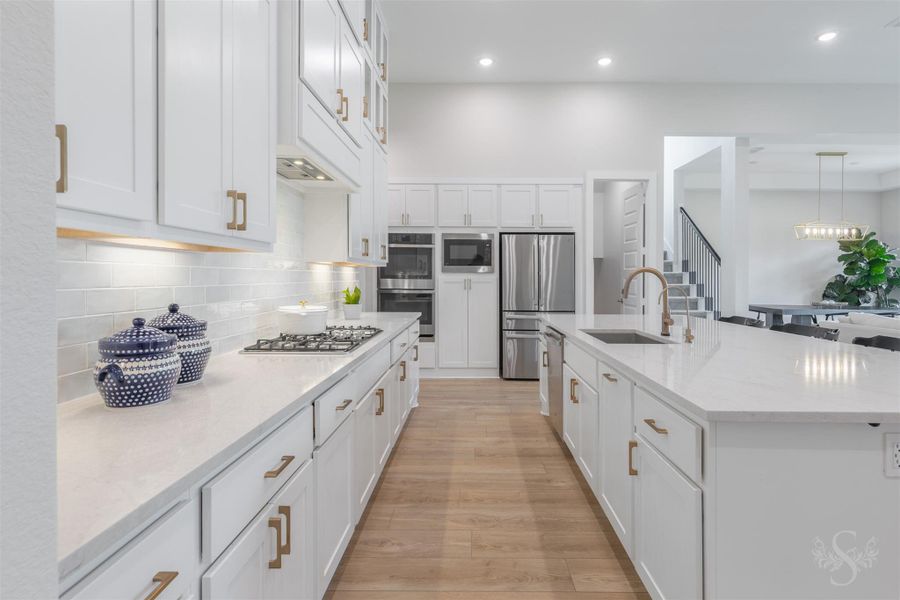 Beautiful white cabinetry offers an exceptional amount of storage, complemented by quartz counters and an elegant tile backsplash. Under-cabinet lighting beautifully highlights the backsplash and warm gold hardware. Beautiful white cabinetry offers an exceptional amount of storage, complemented by quartz counters and an elegant tile backsplash. Under-cabinet lighting beautifully highlights the backsplash and warm gold hardware.