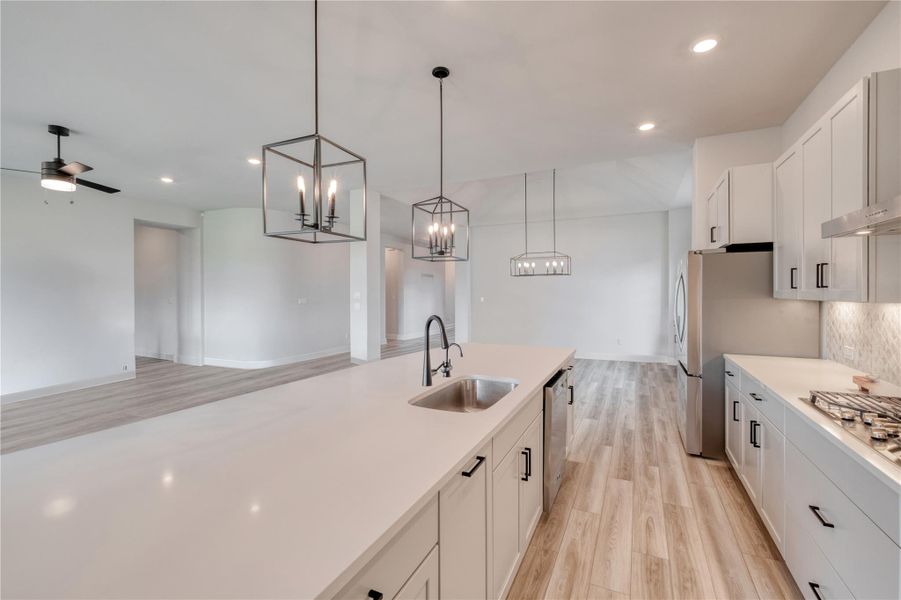 Open-concept kitchen featuring a spacious island with sink, stainless steel appliances, white cabinetry with black hardware, and wood-finish flooring