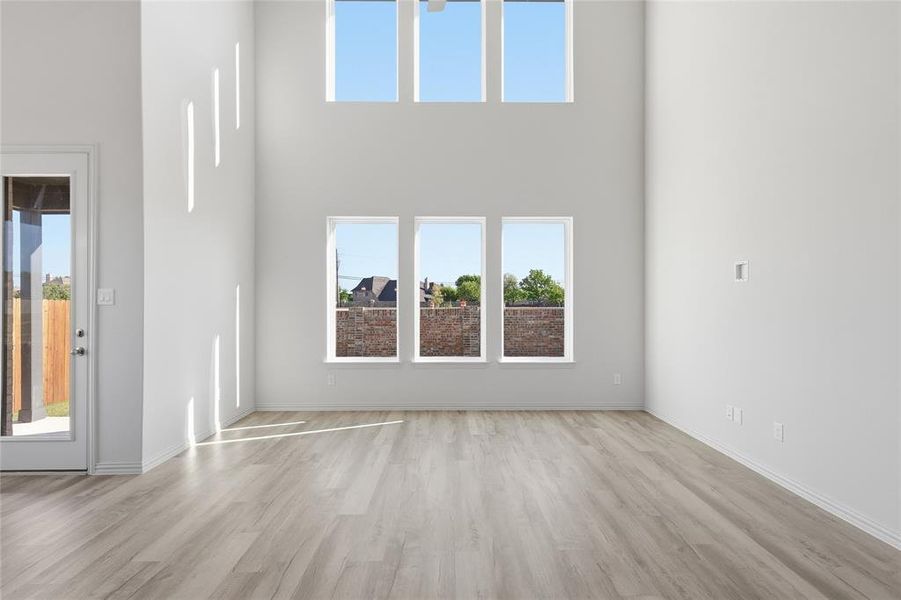 Unfurnished living room featuring healthy amount of natural light, light wood-style floors, and a high ceiling Unfurnished living room featuring healthy amount of natural light, light wood-style floors, and a high ceiling