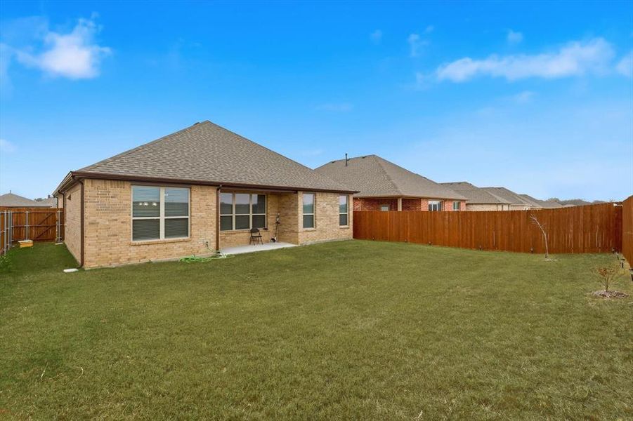 Rear view of house with brick siding, a shingled roof, a patio, and a fenced backyard