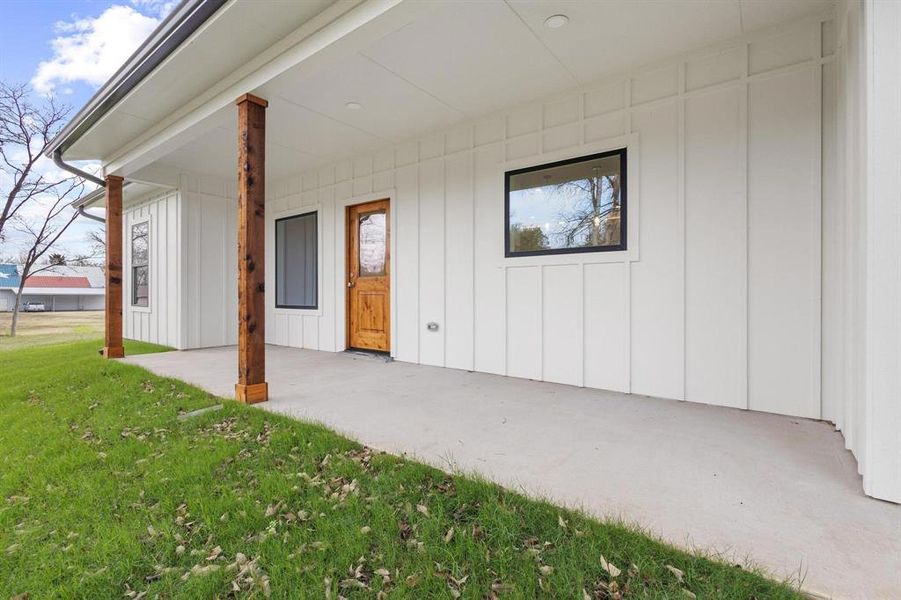 Property entrance with board and batten siding, a yard, and a patio