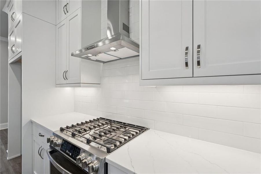 Kitchen with gas stove, extractor fan, white cabinets, and light stone countertops