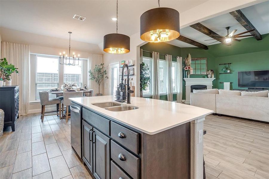 Kitchen with ceiling fan with notable chandelier, decorative light fixtures, light hardwood / wood-style flooring, beamed ceiling, and an island with sink