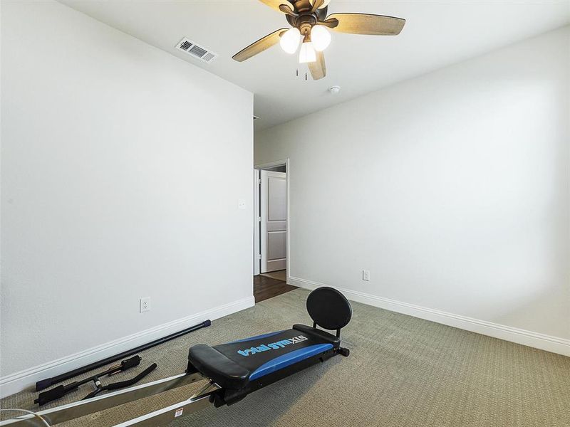 Bedroom currently used as workout room with light carpet and ceiling fan