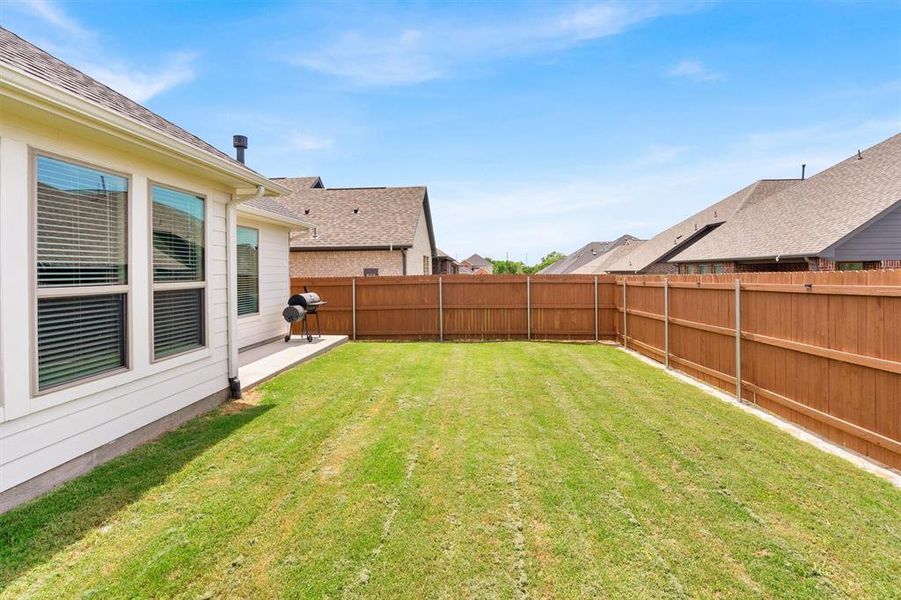 Expansive backyard featuring a lush lawn, solid wood privacy fencing, and a concrete patio space