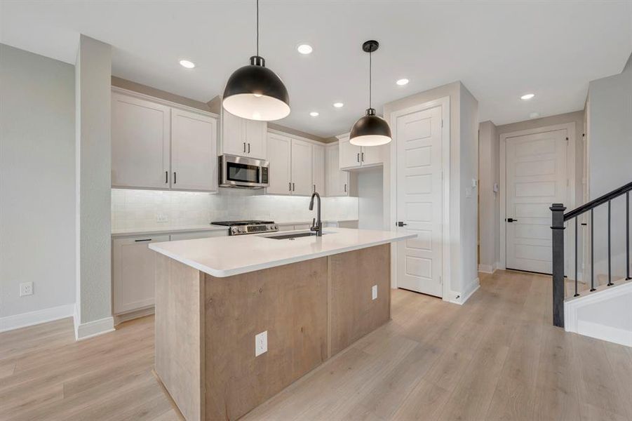Kitchen featuring stainless steel appliances, an island with sink, light wood-type flooring, pendant lighting, and tasteful backsplash