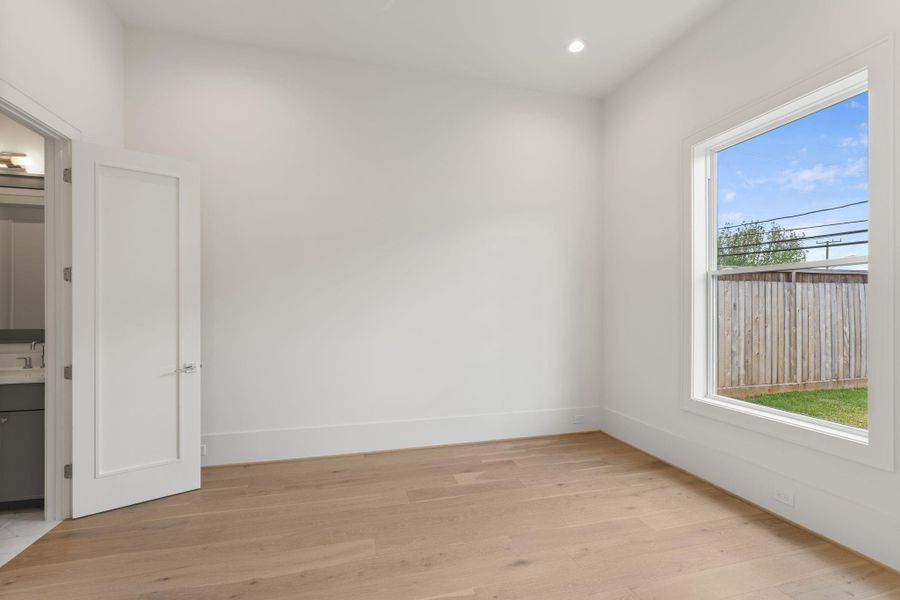 A spacious secondary bedroom features large windows, wide-plank flooring, and a neutral palette, offering flexibility for guests or additional living space.