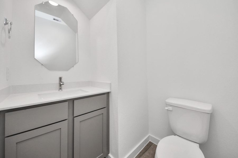 Sophisticated half bathroom adorned with contemporary finishes. The elegant 5-panel door welcomes you to a space where style meets functionality. Notice the sleek hardware accents that add a touch of modern charm. The vanity boasts light-colored countertops, beautifully complemented by a tasteful recessed light, creating a well-lit and inviting atmosphere. Sample photo of completed home with similar floor plan. Actual colors and selections may vary.