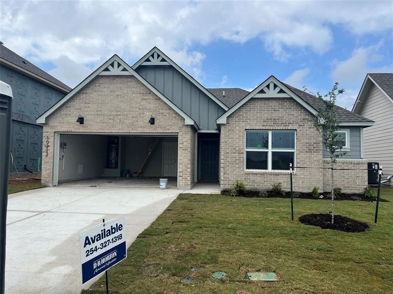 Craftsman-style home featuring an attached garage, driveway, a front yard, board and batten siding, and brick siding Digital R