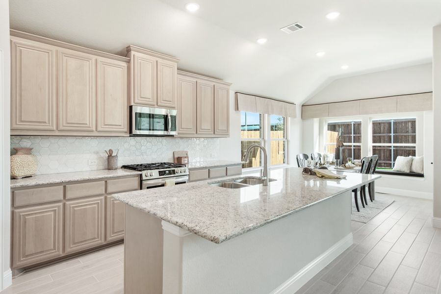 Kitchen with large granite island, beige cabinets, stainless steel appliances, and tile backsplash open to dining area Kitchen with large granite island, beige cabinets, stainless steel appliances, and tile backsplash open to dining area