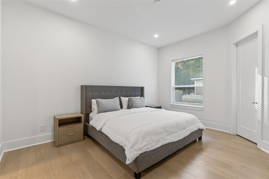Additional bedroom features warm flooring, a spacious layout, and a window overlooking the property. **Images are from a previously completed project. **