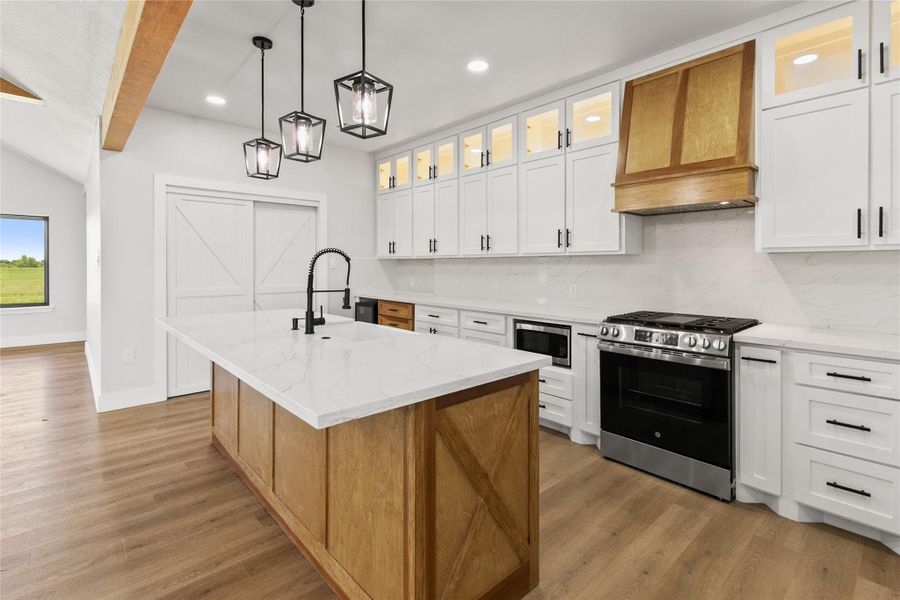The kitchen blends style and function with quartz countertops, a wood island with an apron-front farmhouse sink, beverage refrigerator, wine storage, under-counter microwave, lighted glass-front cabinetry, and a large walk-in pantry.