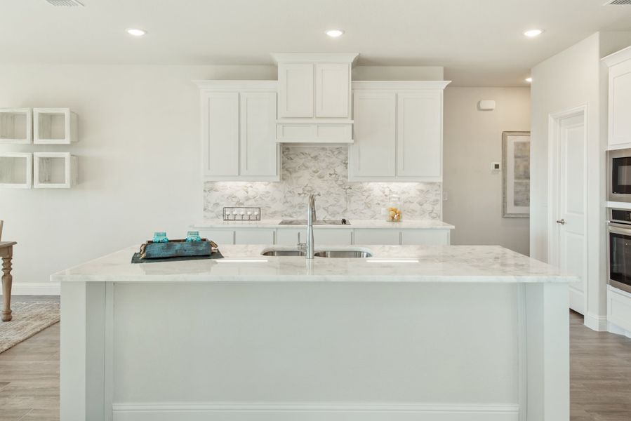 Kitchen island with double sink, white cabinets, marble backsplash, and light wood floors