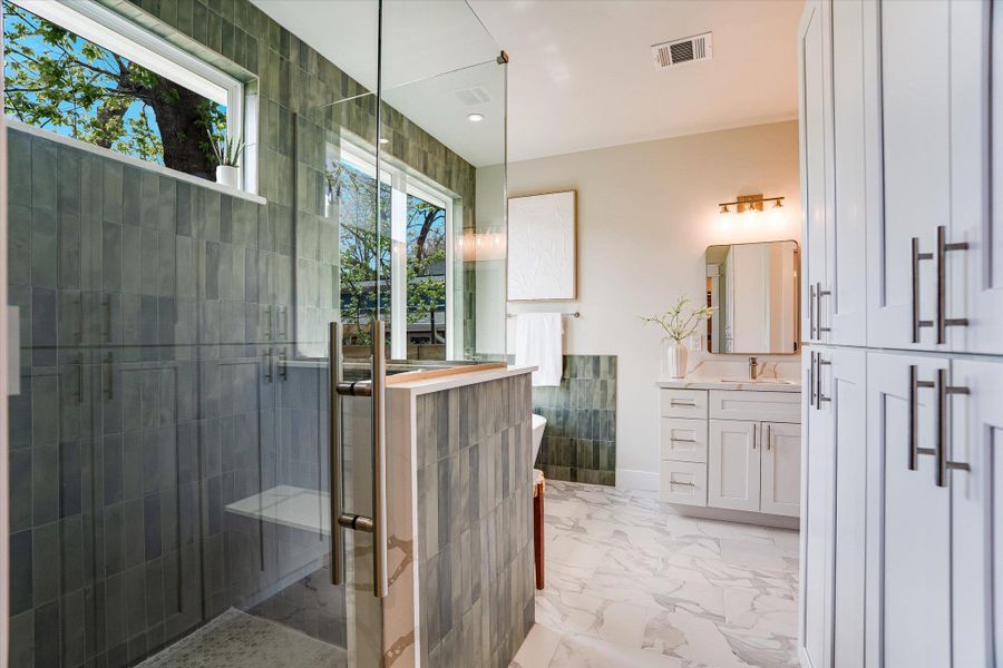 Bathroom with a glass-enclosed shower featuring dark gray tile, a white vanity with a rectangular sink and mirror, and built-in white cabinetry with dark handles Bathroom with a glass-enclosed shower featuring dark gray tile, a white vanity with a rectangular sink and mirror, and built-in white cabinetry with dark handles