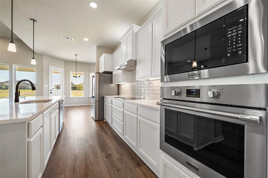 Kitchen featuring appliances with stainless steel finishes, white cabinets, decorative light fixtures, dark wood-style floors, and tasteful backsplash