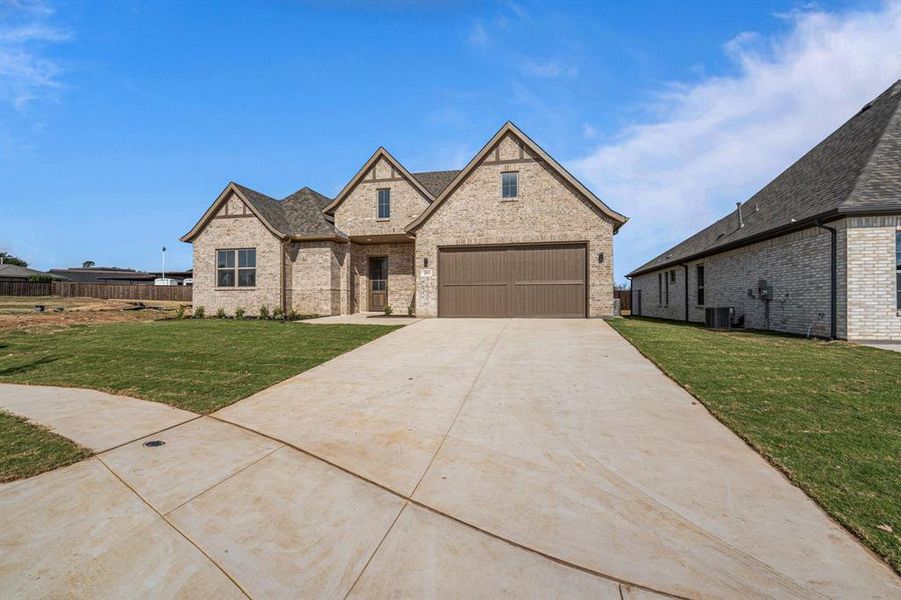 French country home with concrete driveway, brick siding, and a garage French country home with concrete driveway, brick siding, and a garage