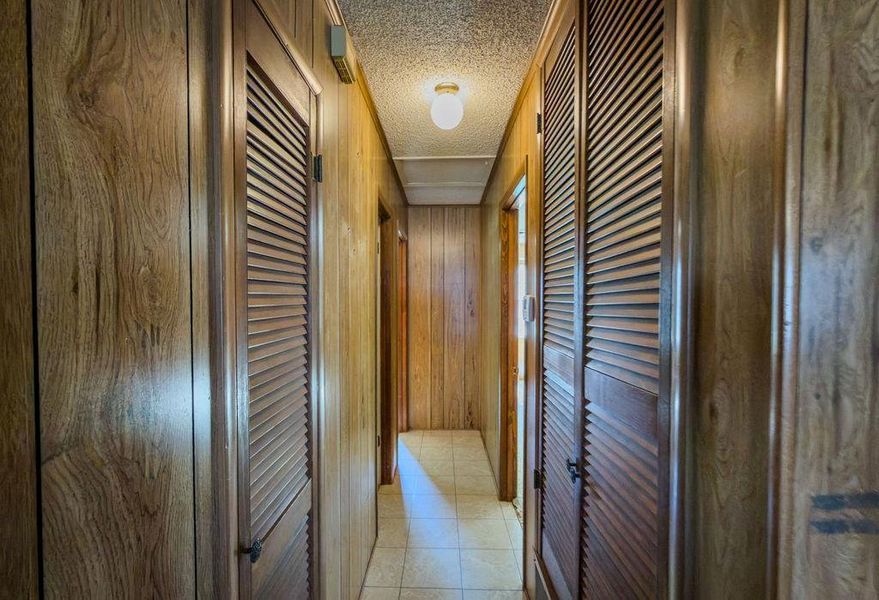 Corridor featuring wood walls, a textured ceiling, and light tile patterned floors