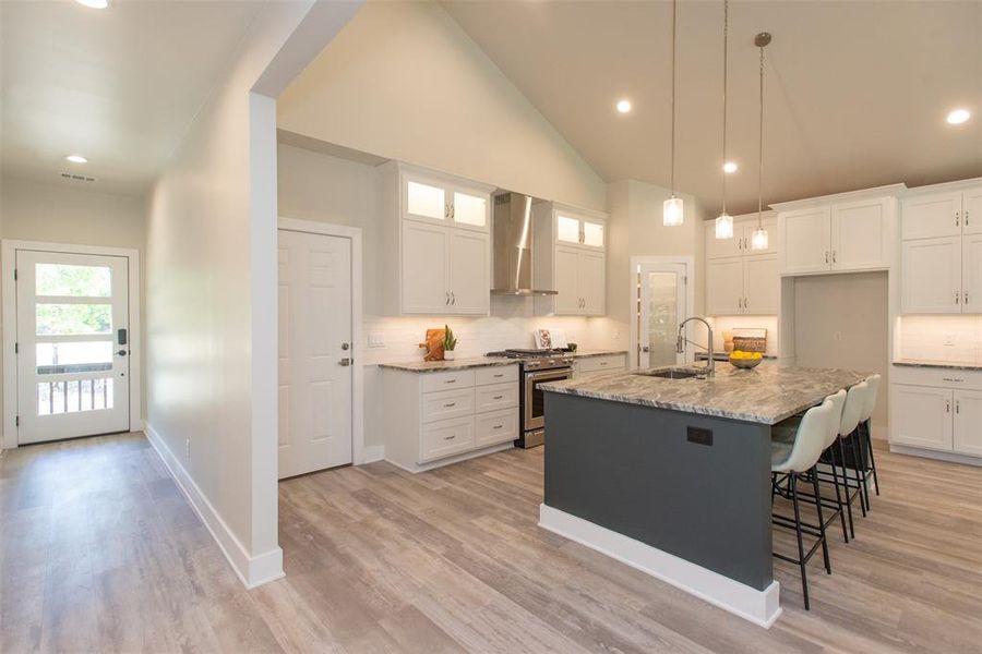 Kitchen featuring custom cabinetry, an island with sink, high end stove, wall chimney exhaust hood, and sink