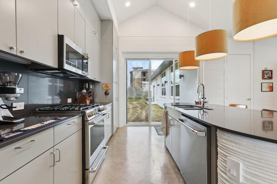 Kitchen featuring stainless steel appliances, finished concrete flooring, vaulted ceiling, decorative light fixtures, and modern cabinets