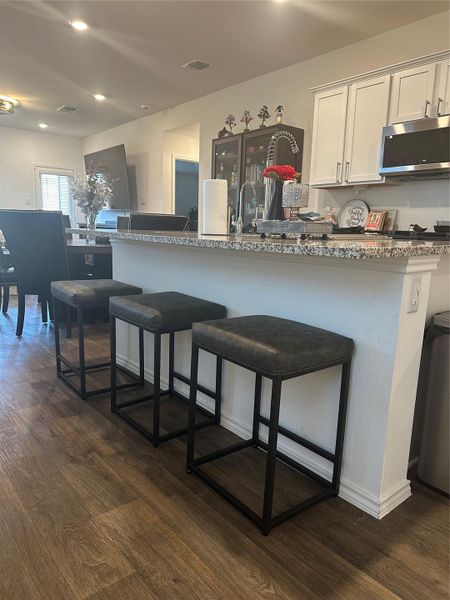 Kitchen with white cabinetry, a breakfast bar, stainless steel microwave, dark wood-style flooring, and light stone countertops