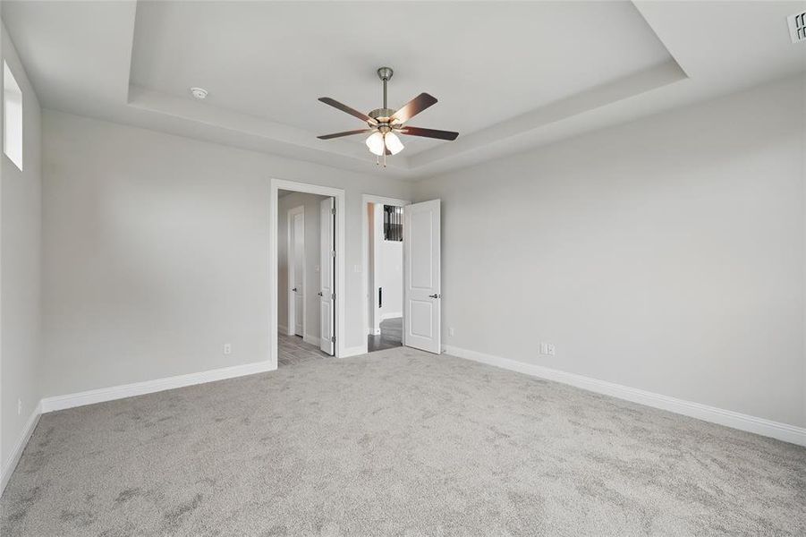 Unfurnished bedroom featuring a raised ceiling, carpet flooring, baseboards, and a ceiling fan Unfurnished bedroom featuring a raised ceiling, carpet flooring, baseboards, and a ceiling fan
