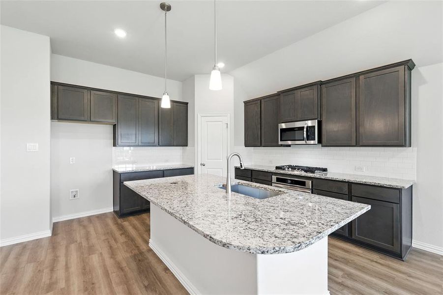 Kitchen with light wood-style floors, dark brown cabinets, light stone counters, backsplash, and recessed lighting