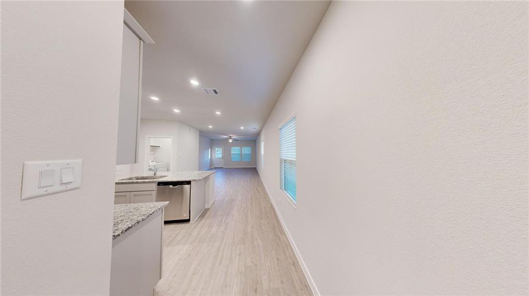 This photo showcases a bright, open-plan interior with wood-style flooring. The kitchen features granite countertops and stainless steel appliances, leading to a spacious living area with recessed lighting and large windows for natural light.