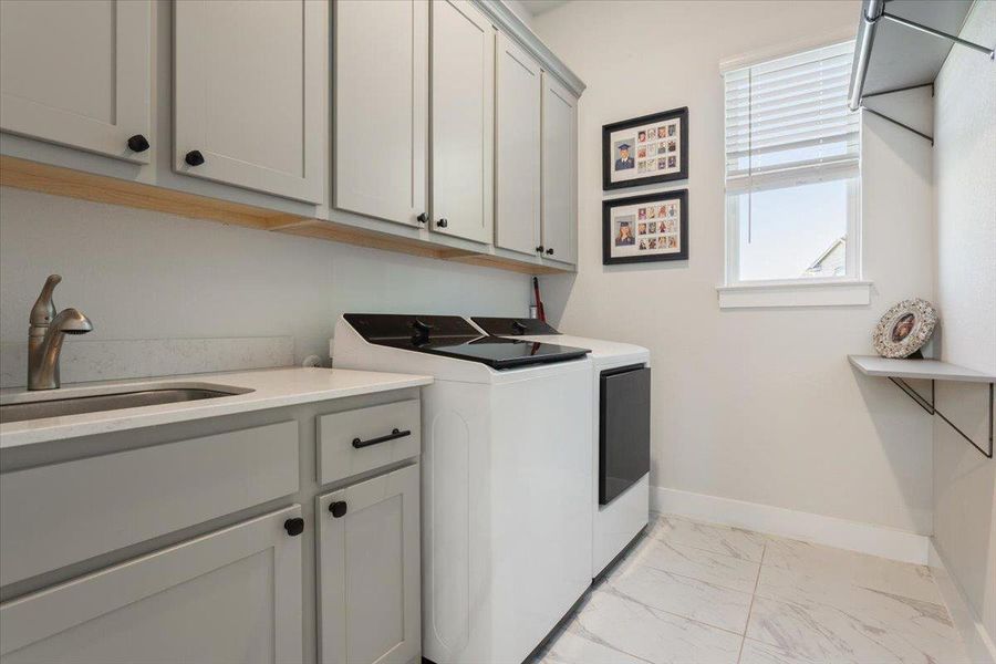 Laundry area featuring light marble finish flooring, washing machine and clothes dryer, and cabinet space