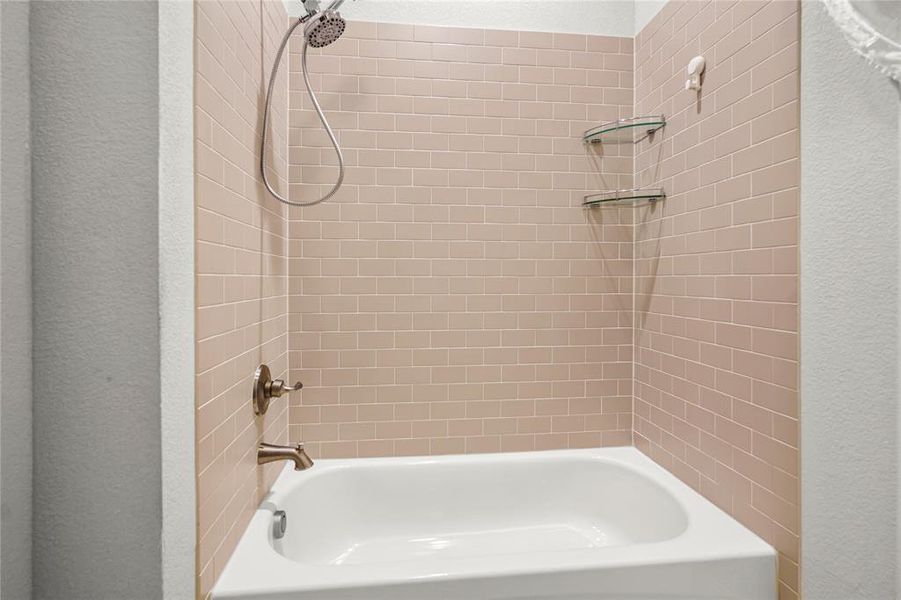 Bathroom featuring washtub / shower combination and a textured wall Bathroom featuring washtub / shower combination and a textured wall