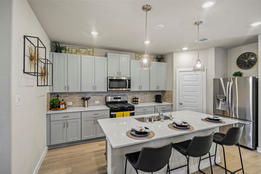Modern kitchen featuring sleek gray cabinetry, stainless steel appliances, and a spacious island with bar seating, complemented by stylish pendant lighting and warm wood flooring.