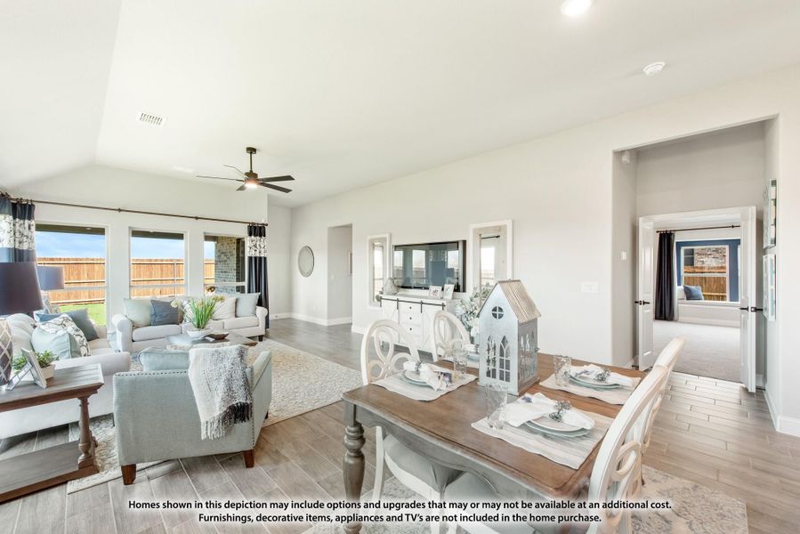 Open-concept living and dining area with vaulted ceiling, ceiling fan, hardwood floors, and large windows overlooking backyard.