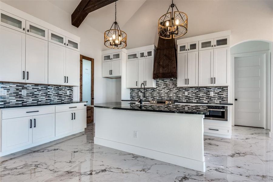 Kitchen with a kitchen island with sink, beamed ceiling, pendant lighting, white cabinets, and high vaulted ceiling