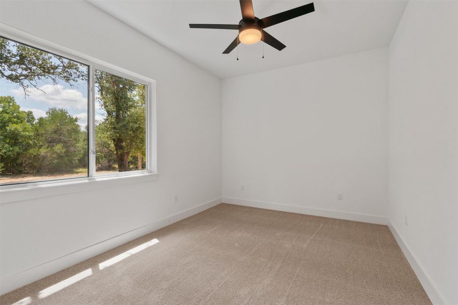 A spacious bedroom offers a large window with peaceful tree-lined views, complementing the neutral carpeting and ceiling fan for comfort.