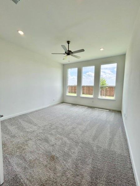 Spacious interior room featuring plush gray carpeting, three large windows, a ceiling fan, and recessed lighting Spacious interior room featuring plush gray carpeting, three large windows, a ceiling fan, and recessed lighting