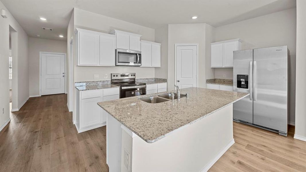Kitchen featuring stainless steel appliances, white cabinets, light stone counters, light wood-style flooring, and a kitchen island with sink