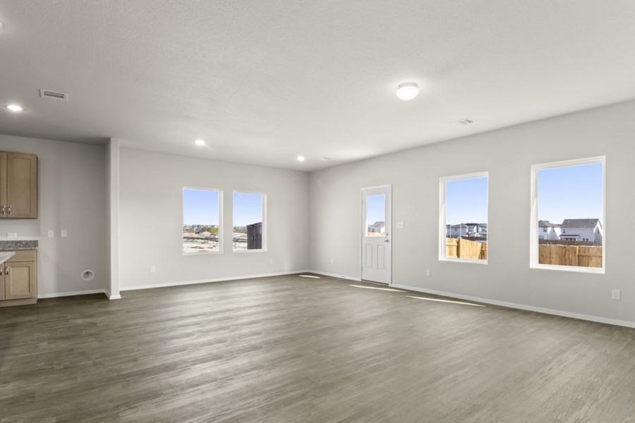 Image of a living room with light grey walls, brown vinyl flooring, windows and a back door