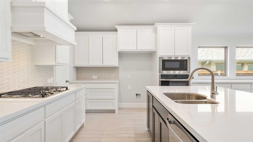 Kitchen with white cabinetry, light hardwood / wood-style flooring, stainless steel appliances, sink, and custom range hood