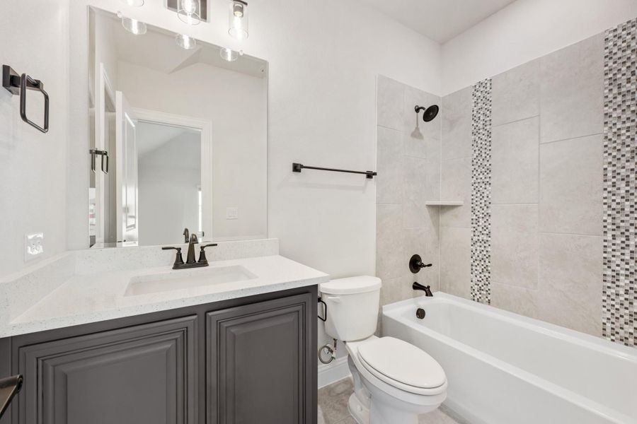Bathroom with gray vanity, quartz countertop, and tiled tub-shower combo with mosaic accent strip Bathroom with gray vanity, quartz countertop, and tiled tub-shower combo with mosaic accent strip