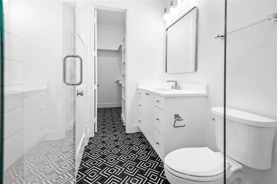 Modern bathroom featuring black and white patterned floor tile, white vanity with integrated sink, rectangular framed mirror, and glass shower enclosure Modern bathroom featuring black and white patterned floor tile, white vanity with integrated sink, rectangular framed mirror, and glass shower enclosure