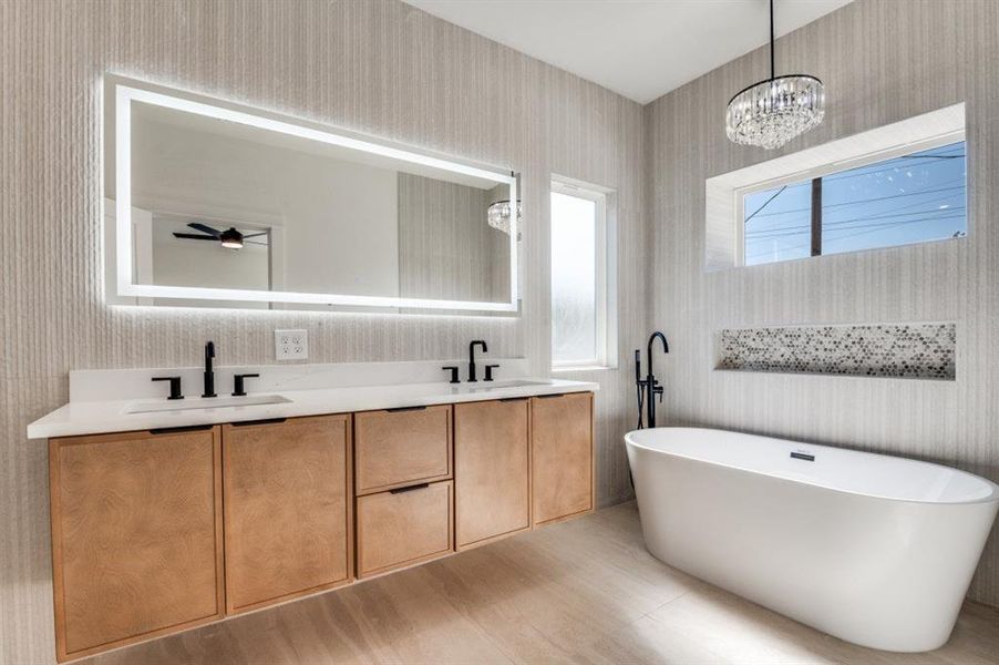 Full bathroom featuring wallpapered walls, a freestanding bath, double vanity, and a chandelier