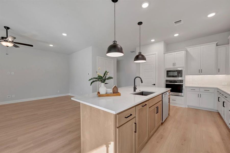 Kitchen with a kitchen island with sink, stainless steel appliances, hanging light fixtures, tasteful backsplash, and light wood-type flooring