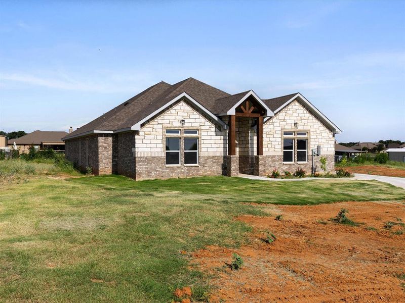 View of front of home featuring brick siding, a front lawn, roof with shingles, and stone siding